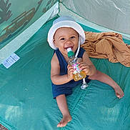 Aaron participe au concours pour gagner de l'argent avec cette photo : toddler, child, smiling, hat, bottle, tent, outdoor, play, happy, sitting, clothing, sunhat, baby, plastic_bottle, fabric, green, blue, summer, daylight, fun
