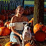 Stella is registered to the contest to win money with this photo: woman, dog, pumpkin, pumpkin_patch, fall, autumn, outdoor, smile, glasses, off_shoulder_top, jeans, bandana, leash, tree, fence, sunlight, grass, hay, sitting, portrait