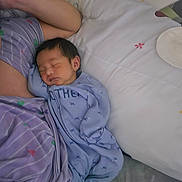 Ezekiel joined the competition — help win amazing prizes! baby, sleeping, newborn, infant, pillow, blanket, purple_clothing, blue_onesie, heart_pattern, flower_pattern, bed, resting, peaceful, indoor, person, skin, head, face, soft_lighting, cozy