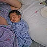 baby, sleeping, newborn, infant, pillow, blanket, purple_clothing, blue_onesie, heart_pattern, flower_pattern, bed, resting, peaceful, indoor, person, skin, head, face, soft_lighting, cozy