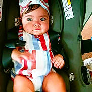 Reyna is registered to the contest to win money with this photo: baby, child, car_seat, striped_clothing, headband, wide_eyes, curious, sitting, safety_harness, infant, indoors, person, cute, chubby_legs, small_hands, colorful, secure, seatbelt, portrait, young