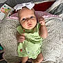 baby, infant, child, pillow, blanket, bow, headband, green_dress, hand, face, blue_eyes, socks, patterned_fabric, baby_wipes, soft_toys, bed, cozy, indoor, portrait, cute