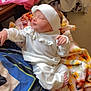 baby, infant, sleeping, white_clothing, headband, blanket, sunflower_pattern, hand, foot, table, pink_shirt, wooden_furniture, indoor, cozy, soft_texture, person, child, cute, resting, peaceful