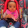 baby, child, car_seat, pink_bib, flower_headband, blue_pants, white_booties, patterned_fabric, indoor, sitting, infant, cute, person, young_child, seatbelt, clothing, portrait, looking_at_camera, adorable, closeup
