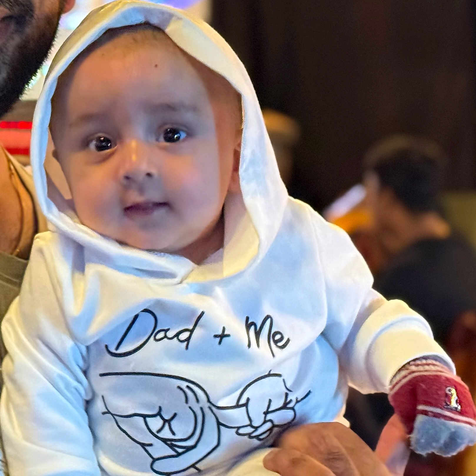 Kabir joined the competition — help win amazing prizes! adult, baby, background_blur, casual, child, cute, expression, face, glove, hand, holding, hoodie, indoor, infant, person, portrait, red_glove, text_on_clothing, warm, white_clothing