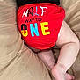 baby, infant, diaper, red_clothing, text_on_clothing, legs, feet, cushion, beige, soft_surface, sleeping_baby, close_up, child, cute, chubby_legs, comfort, indoor, relaxing, colorful_text, halfway_to_one