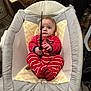 baby, infant, pajamas, red_stripes, baby_rocker, cushion, indoor, flooring, dog, toy, person, hand, face, expression, footwear, furniture, household, curious, child, grip