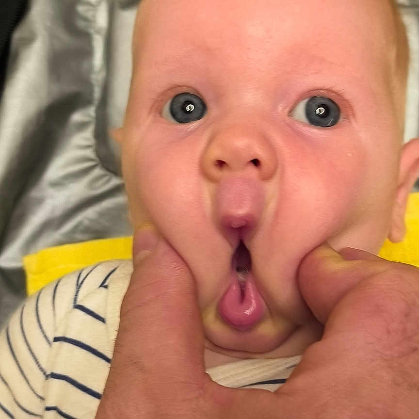 Tòr a rejoint le concours — aidez-le/la à gagner de superbes lots ! adult_hand, baby, bedding, blue_eyes, child, closeup, cute, face, fingers, hands, indoor, infant, mouth, portrait, skin, striped_onesie, surprised_expression, towel, travel_bag, wooden_floor