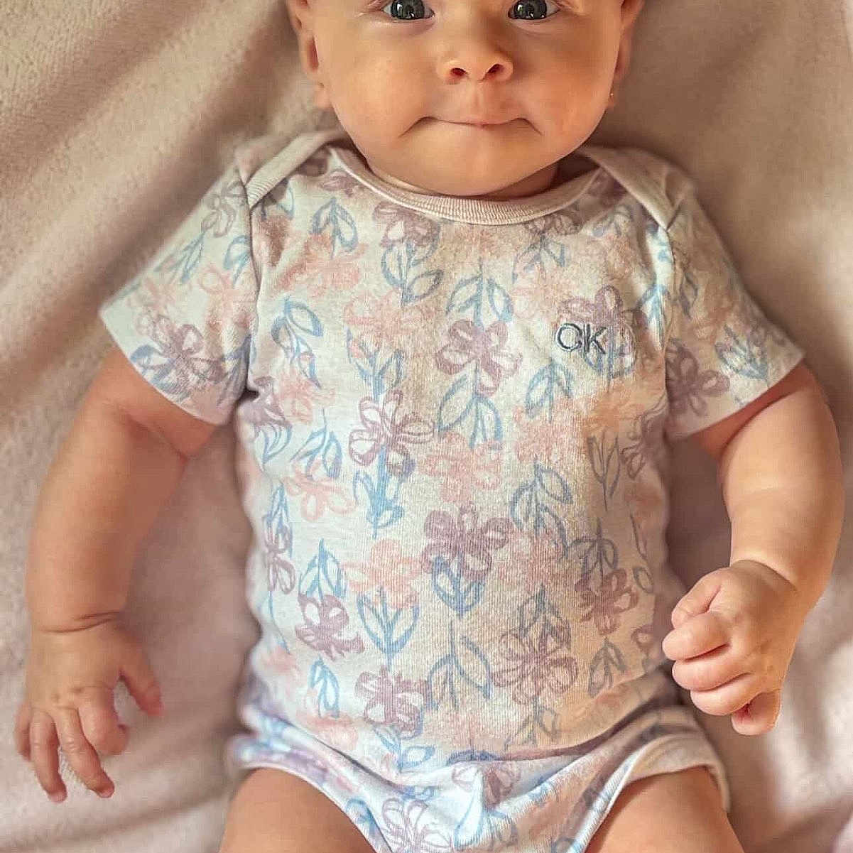 Malena is registered to the contest to win money with this photo: arms, baby, blanket, child, comfort, cute, expression, face, floral_pattern, indoors, infant, legs, lying_down, onesie, person, portrait, skin, smile, soft_texture, young