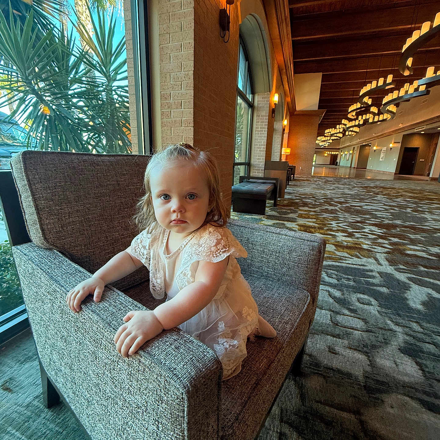 Amelia is registered to the contest to win money with this photo: architecture, armchair, blue_eyes, carpet, child, curious, decor, dress, expression, furniture, hallway, indoor, lace, lighting, natural_light, person, plant, portrait, toddler, window