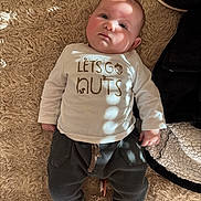 Luna participe au concours pour gagner de l'argent avec cette photo : adorable, baby, carpet, child, clothing, cozy, cute, dark_pants, face, floor, indoor, infant, lying_down, pants, person, shadow, shirt, sock, soft_light, white_shirt