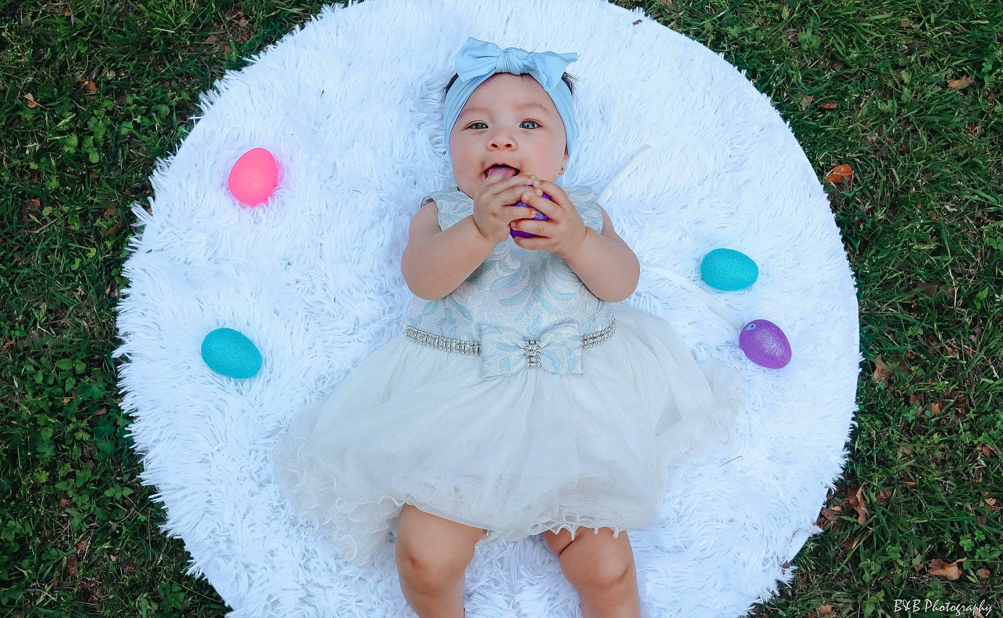 Eva is registered to the contest to win money with this photo: baby, baby_toddler_clothing, dress, eye, facial_expression, grass, hairstyle, happy, head, headgear, headwear, leaf, organ, people_in_nature, person, petal, pink, plant, product, skin