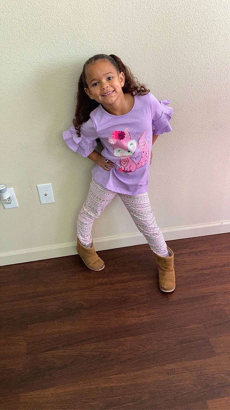 Braylee is registered to the contest to win money with this photo: active_pants, arm, baby_toddler_clothing, floor, flooring, happy, hardwood, human_leg, joy, knee, leg, magenta, person, purple, sleeve, smile, sock, sportswear, t_shirt, thigh