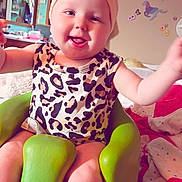 Aurora is registered to the contest to win money with this photo: baby, child, smile, headband, bow, leopard_print, green_chair, indoor, happy, arms_outstretched, cute, infant, room_decor, blanket, wall_stickers, toddler, person, seat, playful, cozy