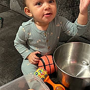 Aurora is registered to the contest to win money with this photo: baby, child, closeup, colorful, curious, expression, gray_couch, hand_raised, home, indoor, long_sleeve_pajamas, metal_bowl, person, pink_bows, plastic_toys, playtime, seated, sunglasses, toddler, toy_basket