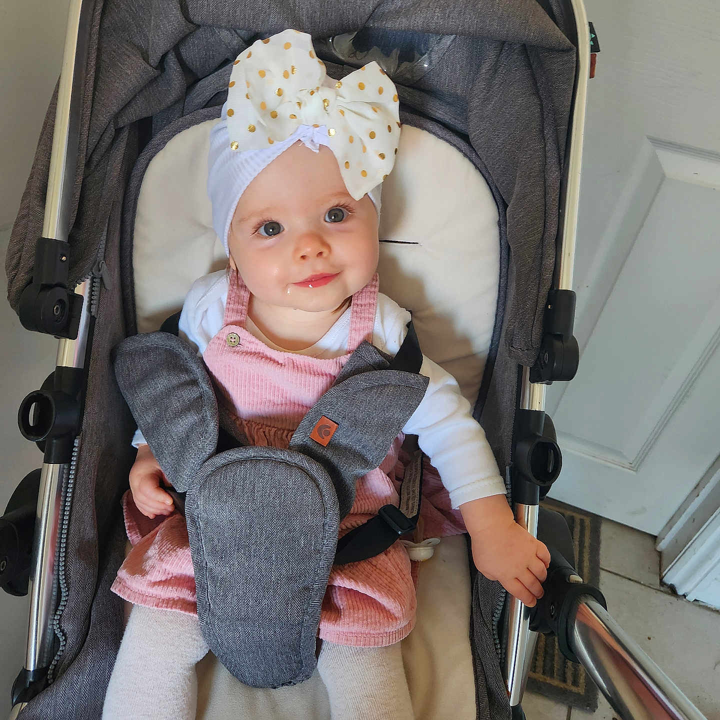 Zoé Lily is registered to the contest to win money with this photo: baby, bow, child, clothing, cute, door, drool, floor_tiles, hand, headband, indoor, infant, metal_frame, person, pink_dress, portrait, seatbelt, smiling, stroller, white_tights