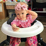Maile is registered to the contest to win money with this photo: baby, child, walker, pink_dress, headband, bow, snack, indoor, carpet, toy, furniture, person, portrait, cute, infant, sitting, expression, face, legs, room