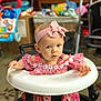 Maile is registered to the contest to win money with this photo: baby, candid, child, curious, expression, floor, floral_outfit, furniture, headband, home, indoor, infant, person, pink_bow, playroom, portrait, seat, snack, toy, walker