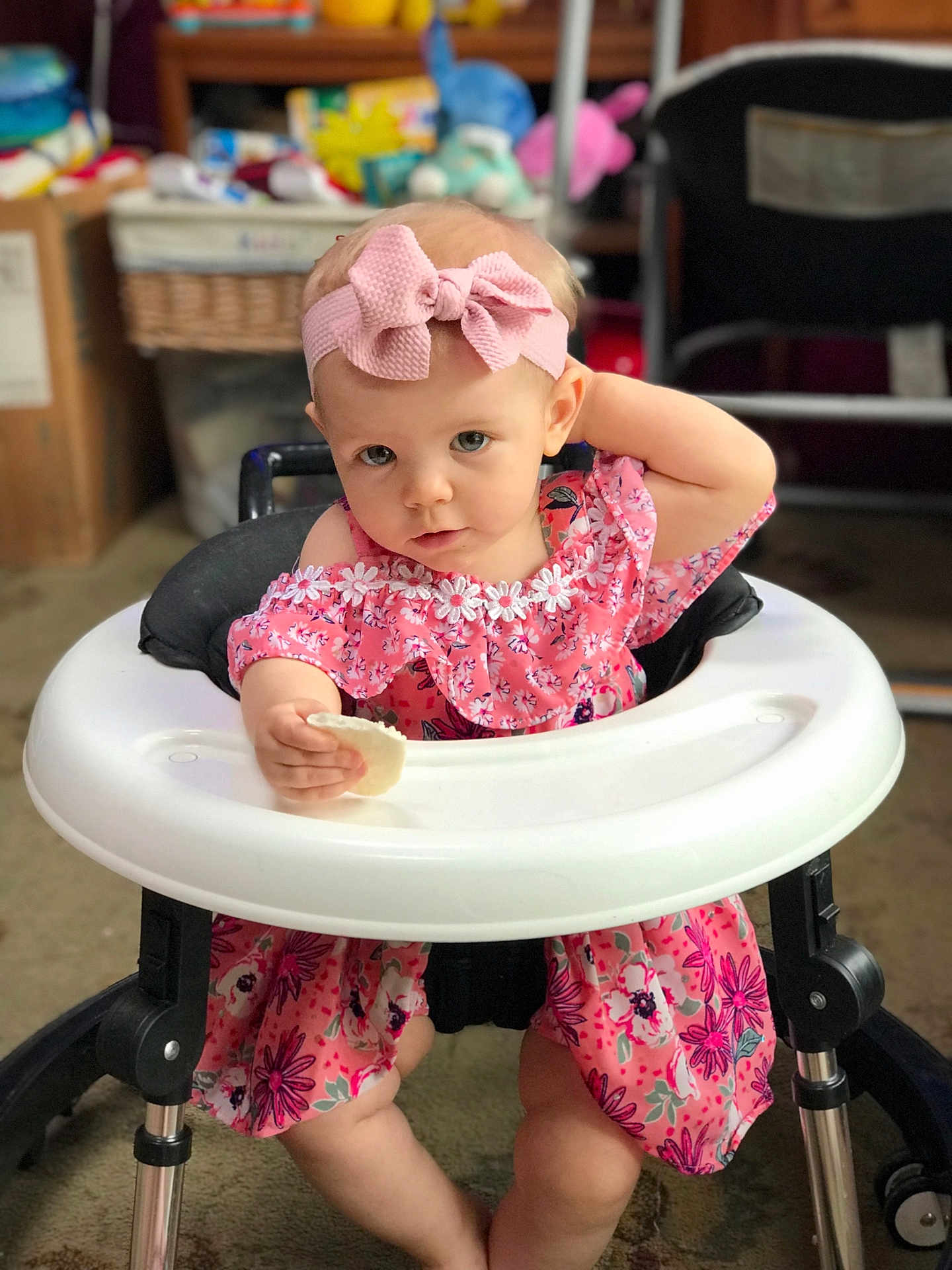 Maile Sue is registered to the contest to win money with this photo: baby, child, pink_dress, headband, bow, walker, snack, indoor, carpet, furniture, toy, person, cute, small_child, seat, hand, legs, expression, face, room