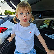 Manon a rejoint le concours — aidez-le/la à gagner de superbes lots ! child, girl, pigtails, blue_eyes, white_tshirt, red_heart, denim_shorts, car_trunk, outdoor, daylight, curious, surprised, standing, casual_clothing, vehicle, nature_background, young_child, portrait, expression, hands