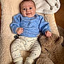 baby, smiling, blue_sweater, patterned_pants, white_socks, teddy_bear_hat, blanket, soft_texture, indoor, happy, child, cute, portrait, cozy, infant, plush, comfortable, seated, warm, furniture
