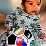 baby, child, soccer_ball, pajamas, stars_pattern, indoor, quilted_blanket, curious, infant, sitting, toy, colorful, sports, face, footwear, sock, young_child, portrait, playing, soft_lighting