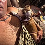 blanket, brown_dog, chain_necklace, comfort, couch, cozy, dog, furniture, hand, human, indoor, leopard_print, man, partial_face, pet, relaxing, resting, short_hair, snuggling, warm_light