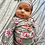baby, infant, floral_outfit, hat, wooden_buttons, blanket, patterned_blanket, lying_down, cute, portrait, child, clothing, headwear, face, small_person, pink_flowers, green_background, soft_light, indoors, adorable