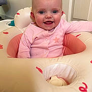 Mia is registered to the contest to win money with this photo: baby, infant, smiling, pink_clothing, inflatable_ring, indoor, child, happy, face, head, person, cute, seated, toy, playtime, young_child, skin, blue_eyes, baby_girl, cozy