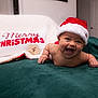 Kassius is registered to the contest to win money with this photo: baby, blanket, celebration, cheerful, child, christmas, cute, decor, face, festive, green_blanket, happy, holiday, holiday_season, indoor, infant, person, santa_hat, smiling, white_blanket