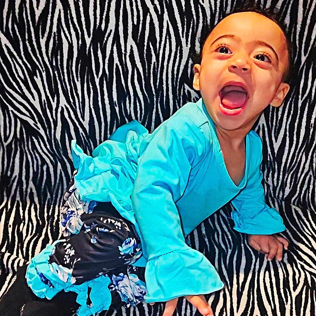 Mya joined the competition — help win amazing prizes! toddler, child, blue_clothing, laughing, crawling, zebra_pattern, background, smile, happy, face, person, indoors, bright_colors, patterned_surface, cute, young_child, black_socks, long_sleeves, playful, expression