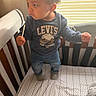 Vega is registered to the contest to win money with this photo: baby, bedding, child, clothing, crib, curly_hair, expression, furniture, hand, indoor, jeans, levis, pattern, person, room, soft_lighting, standing, sweatshirt, toddler, window_blinds