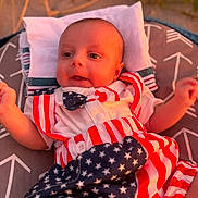 Asaiah joined the competition — help win amazing prizes! arm, baby, blue, bowtie, child, clothing, cushion, face, head, indoors, infant, laying, patriotic, pattern, red, smiling, stars, stripes, warm_light, white