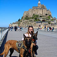 Riley participe au concours pour gagner de l'argent avec cette photo : architecture, belgian_malinois, blue_sky, boardwalk, bridge, daytime, dog, harness, historic_building, leash, mont_saint_michel, nature, outdoor, people, pet, smiling, tourist, travel, walking, woman