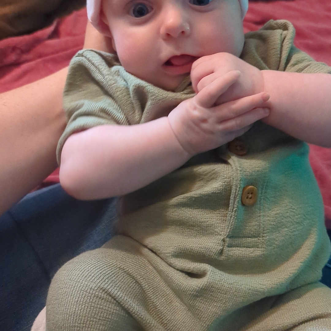 Sylvia joined the competition — help win amazing prizes! arm, baby, clothing, cozy, cute, eyes, face, green_outfit, hands, hat, home, indoors, infant, person, pink_hat, portrait, sitting, soft_fabric, support, young_child