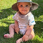 William is registered to the contest to win money with this photo: baby, child, grass, hat, sun_hat, outdoor, summer, greenery, sitting, cute, smile, bib, sunlight, nature, barefoot, infant, clothing, portrait, daylight, young