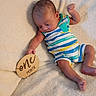 Asher joined the competition — help win amazing prizes! baby, infant, one_month, striped_clothing, romper, blanket, soft_texture, wooden_sign, milestone, newborn, lying_down, hand_raised, curious_expression, cute, child, person, skin, foot, head, small