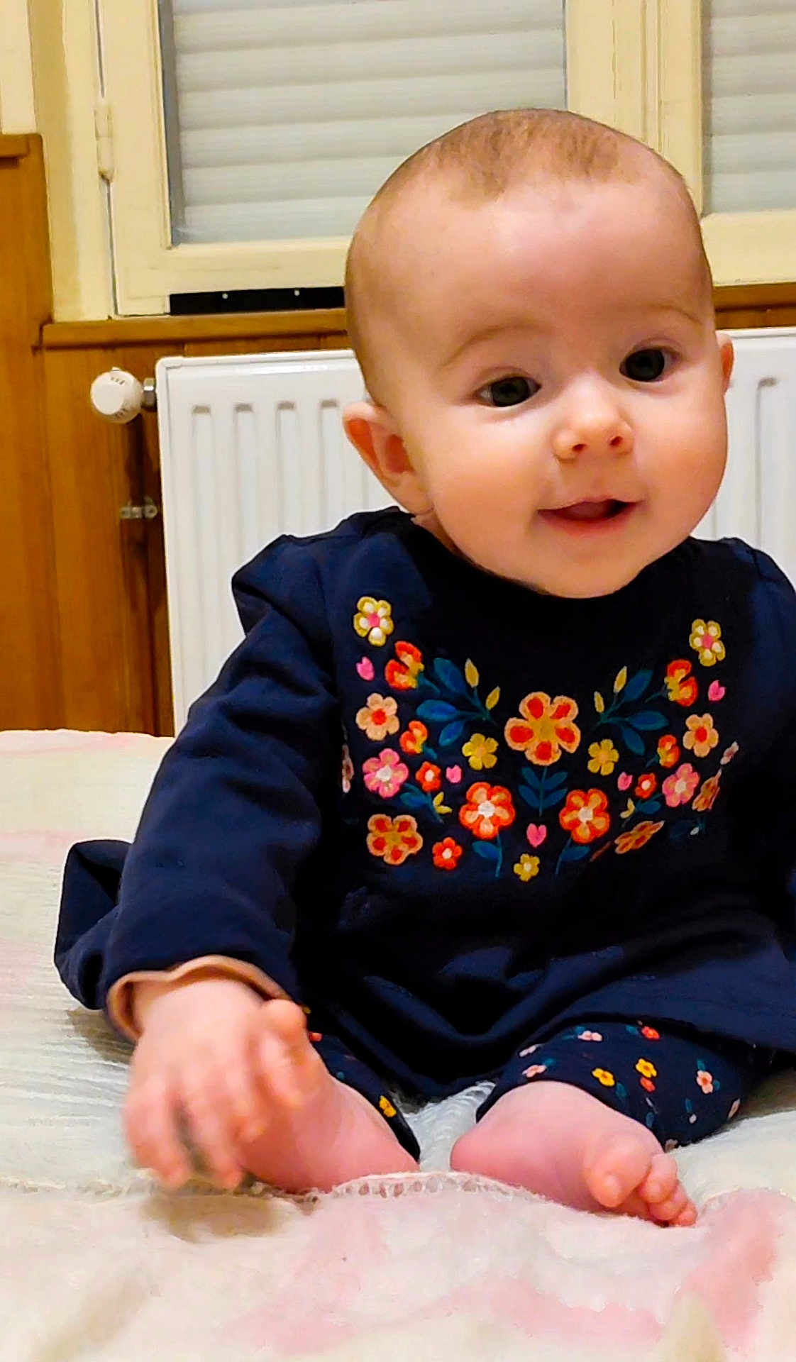 Coraline participe au concours pour gagner de l'argent avec cette photo : baby, infant, child, smiling, sitting, clothing, embroidered_flowers, navy_outfit, feet, hands, indoor, blanket, radiator, window, cute, portrait, face, happy, young_child, cozy