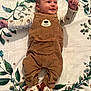 adorable, baby, bear_design, blanket, brown_overalls, buttoned_overalls, child, cute, footwear, happy, indoor, infant, leaf_pattern, long_sleeve_shirt, lying_down, portrait, slippers, small_hands, smiling, soft_texture