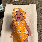 Aila joined the competition — help win amazing prizes! baby, infant, smiling, yellow_clothing, polka_dot, bonnet, lying_down, happy, carpet, white_blanket, cheerful, child, cute, indoors, one_person, small_baby, apparel, headwear, skin, playful