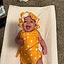 baby, infant, smiling, yellow_clothing, polka_dot, bonnet, lying_down, happy, carpet, white_blanket, cheerful, child, cute, indoors, one_person, small_baby, apparel, headwear, skin, playful