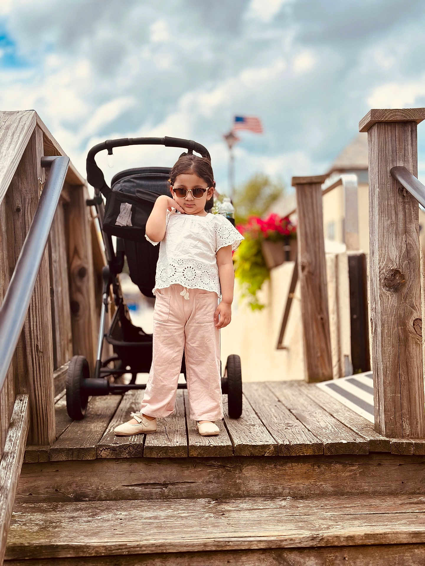Siyara joined the competition — help win amazing prizes! child, toddler, sunglasses, white_top, pink_pants, shoes, stroller, wooden_bridge, handrail, american_flag, cloudy_sky, outdoor, flower_pot, wood, person, fashion, summer, cute, walking, portrait