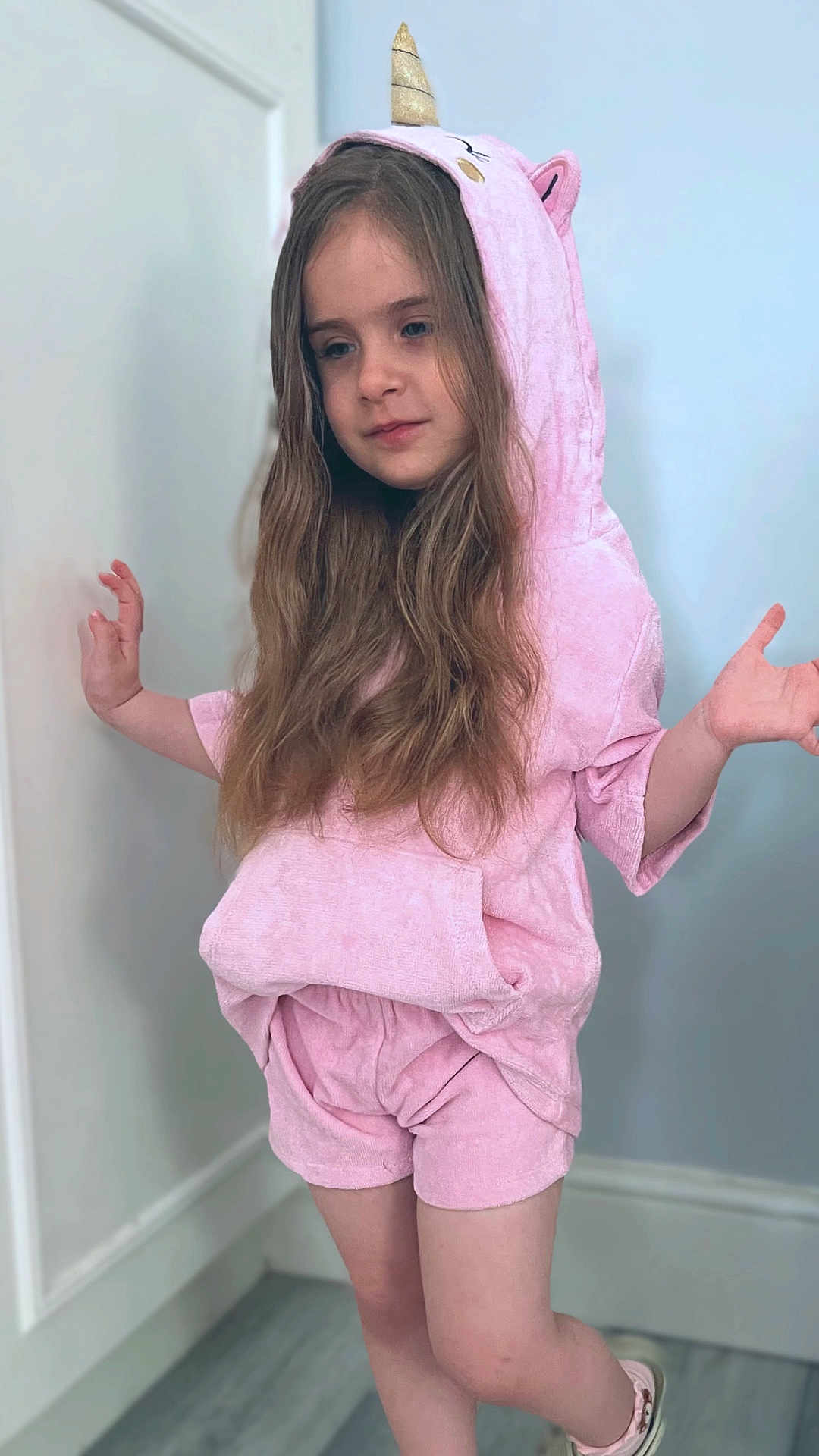 Emma joined the competition — help win amazing prizes! child, pink_clothing, unicorn_hood, hoodie, shorts, long_hair, indoor, pose, playful, casual, footwear, light_blue_wall, white_door, flooring, young_girl, cute, relaxed, portrait, fashion, costume