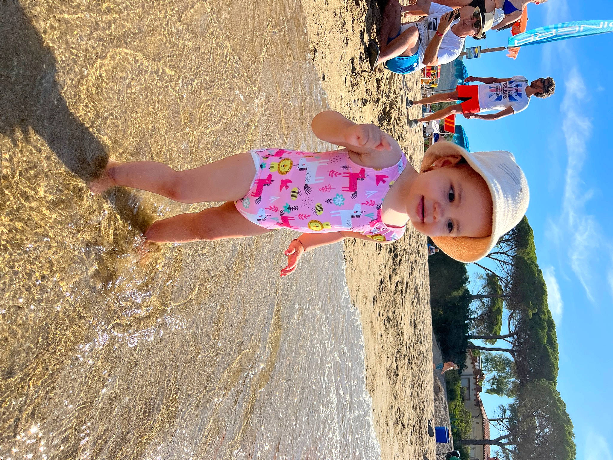 Sienna joined the competition — help win amazing prizes! baby, beach, body_of_water, child, dress, fun, happy, hat, headwear, human_leg, leisure, people_in_nature, person, play, recreation, shadow, sky, soil, thigh, toddler