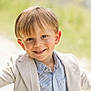 child, boy, smiling, outdoor, portrait, face, light_blazer, striped_shirt, happy, young, cute, casual_wear, sunlight, natural_light, grass_background, blond_hair, short_hair, arms_outstretched, daytime, closeup