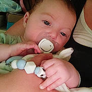 Manoë a rejoint le concours — aidez-le/la à gagner de superbes lots ! adult, arm, baby, background, bracelet, child, closeup, clothing, comfort, face, hand, holding, indoor, infant, pacifier, person, room, skin, soft_toy, toy