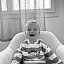 Noah participe au concours pour gagner de l'argent avec cette photo : child, boy, smiling, curly_hair, striped_sweater, text_on_clothing, armchair, indoor, black_and_white, window, curtains, happy, portrait, casual_clothing, seated, young_boy, cozy, home, toddler, person