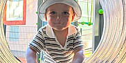 Noah a rejoint le concours — aidez-le/la à gagner de superbes lots ! toddler, child, hat, striped_shirt, playground, tunnel, outdoor, hands, face, smile, person, window, building, daylight, fence, play_equipment, curious, cute, young_child, casual_clothing