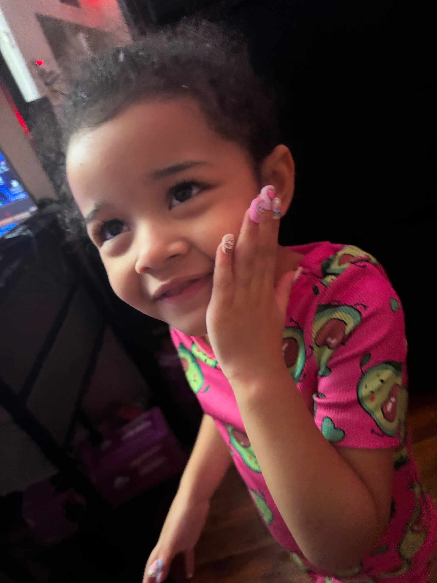 Iris is registered to the contest to win money with this photo: child, smiling, pink_shirt, avocado_pattern, hand_on_face, curly_hair, nails, indoor, portrait, person, happy, cute, young, girl, face, skin, wood_floor, furniture, dim_light, casual_clothing