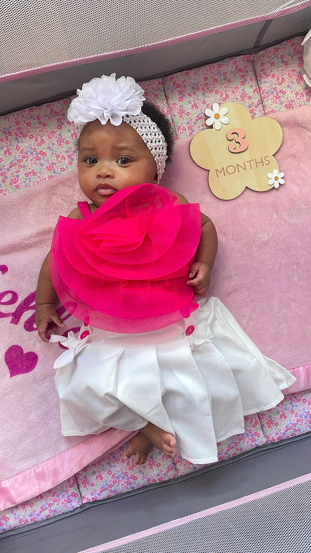 Kehlani joined the competition — help win amazing prizes! baby, infant, girl, headband, flower, pink, white, dress, blanket, playpen, milestone, wooden_sign, 3_months, cute, portrait, laying_down, indoors, child, smiling, face